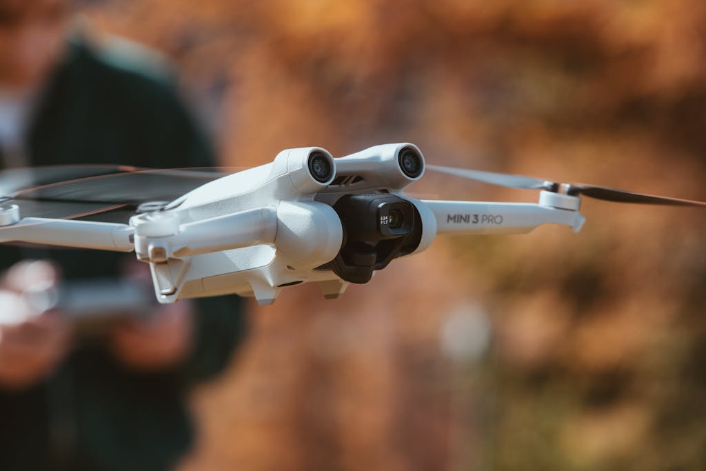 A detailed close-up of a white drone flying outdoors against a fall backdrop.