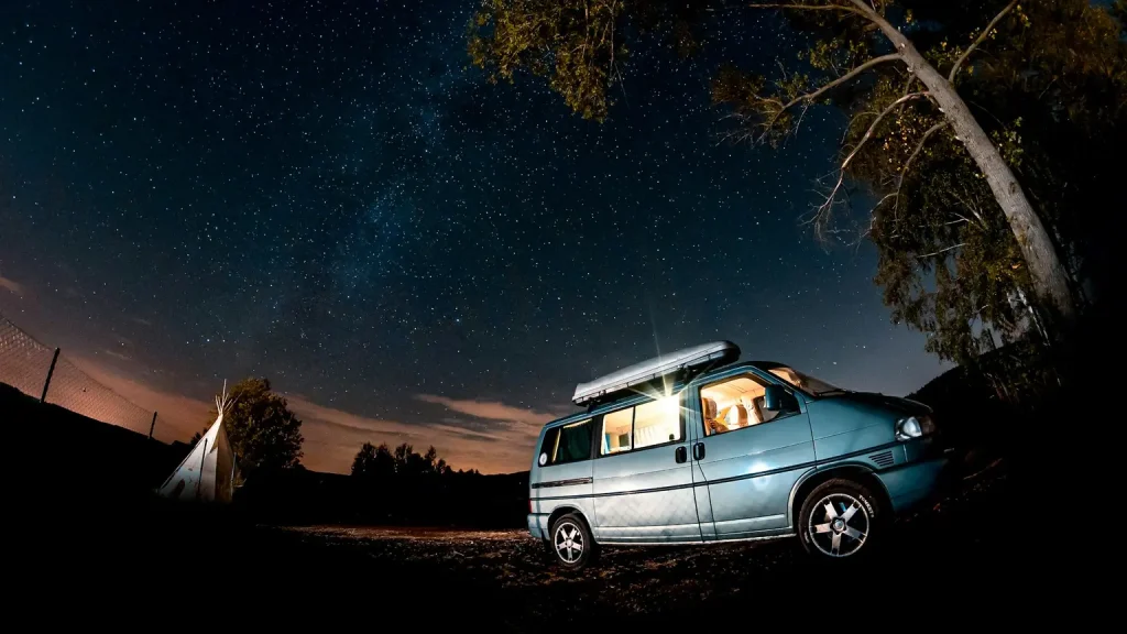 Beleuchteter Campervan unter einem klaren Sternenhimmel bei Nacht