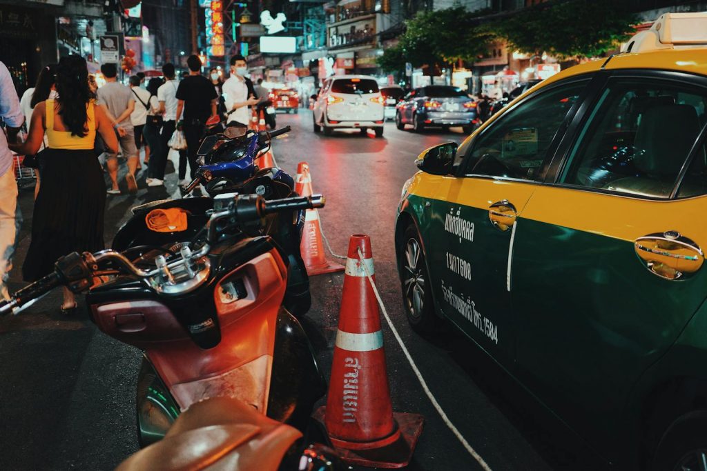 Lively urban street filled with people, taxis, motorcycles, and neon lights at night.