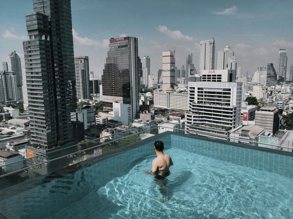 Mann im Rooftop Pool mit Blick auf die Skyline von Bangkok