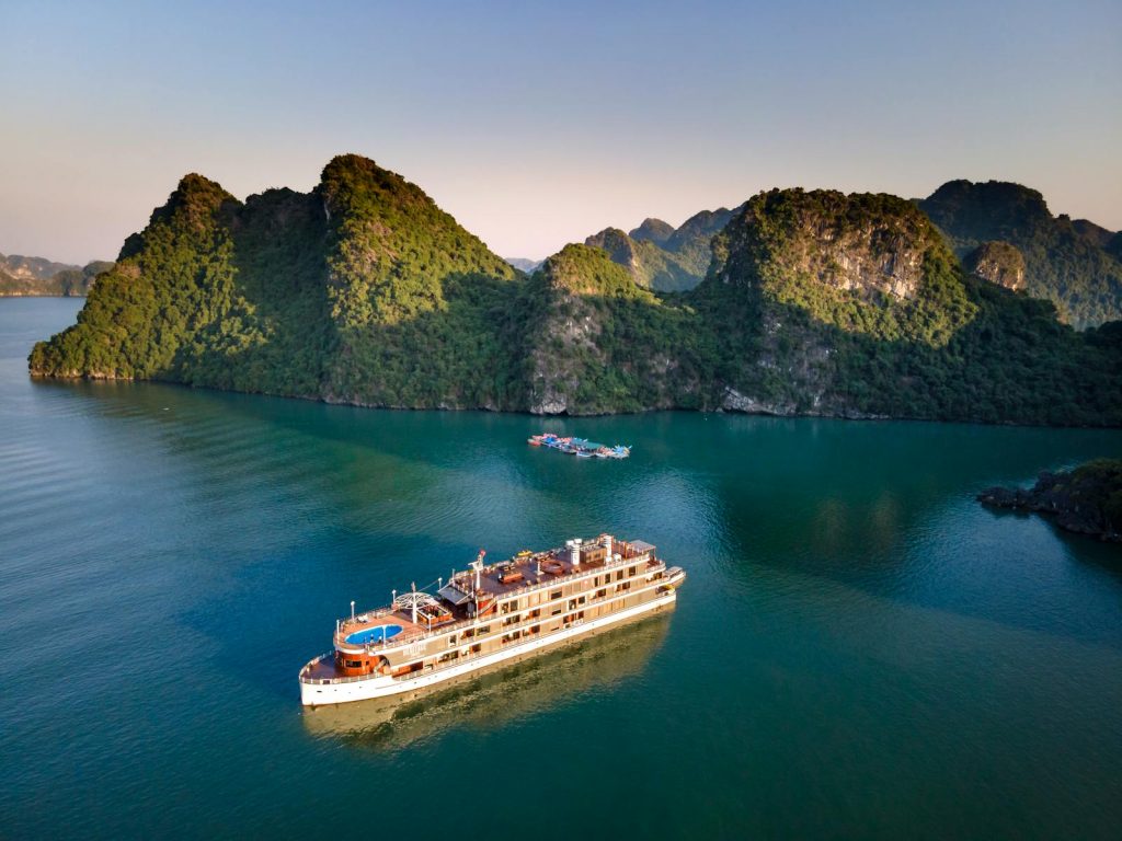 A cruise ship navigates the tranquil waters of Halong Bay with stunning limestone cliffs in the background.