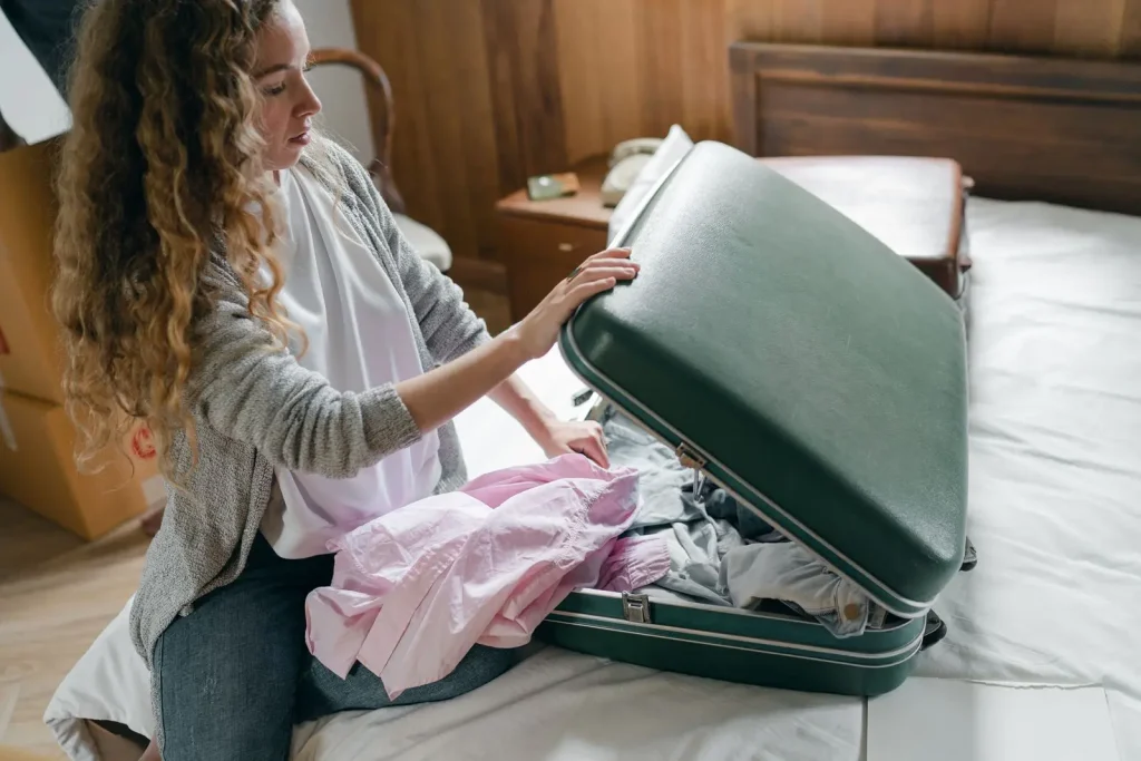 Frau packt einen grünen Koffer auf einem Bett