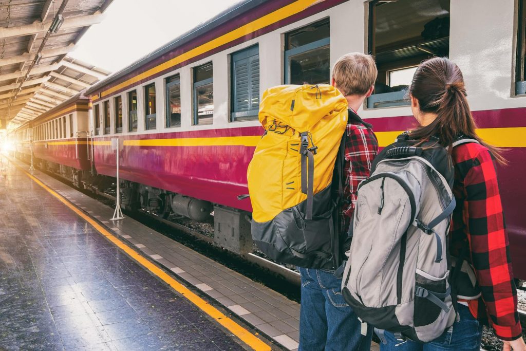Zwei Backpacker warten mit ihren Rucksäcken an einem Bahnhof in Thailand