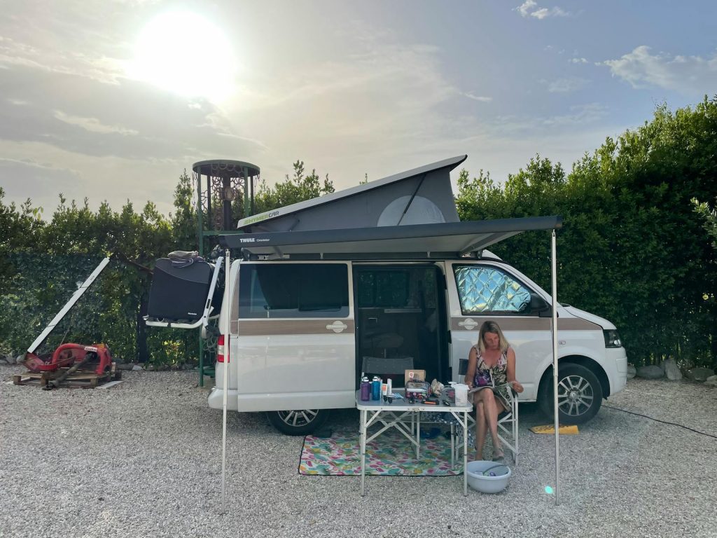 Woman relaxing outside a camper van in Ripatransone, Italy, during a sunny day.