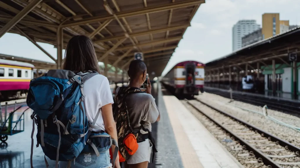 Reisende mit Reiserucksack und Rollkoffer am Bahnhof