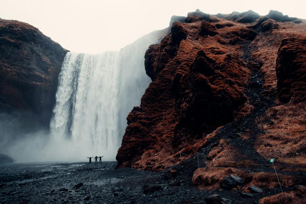 A group of adventurers stands before the majestic Skogafoss waterfall in Iceland.