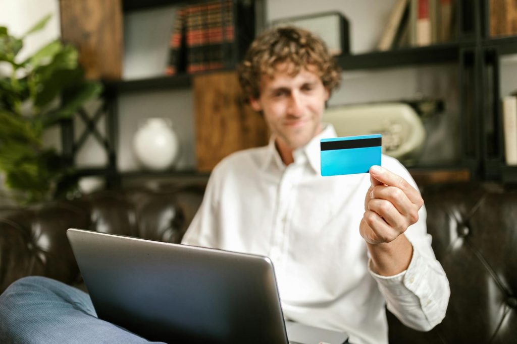 Mann sitzt auf dem Sofa und hält Kreditkarte für Onlinezahlung