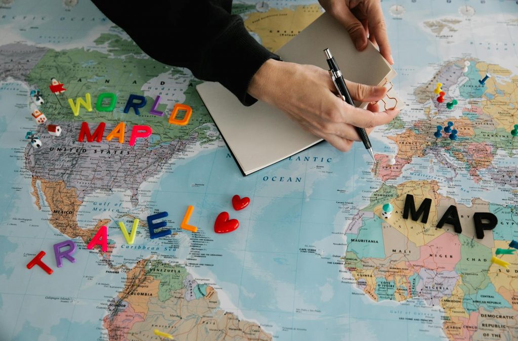 Hands holding pen and notebook over vibrant world map planning a journey.