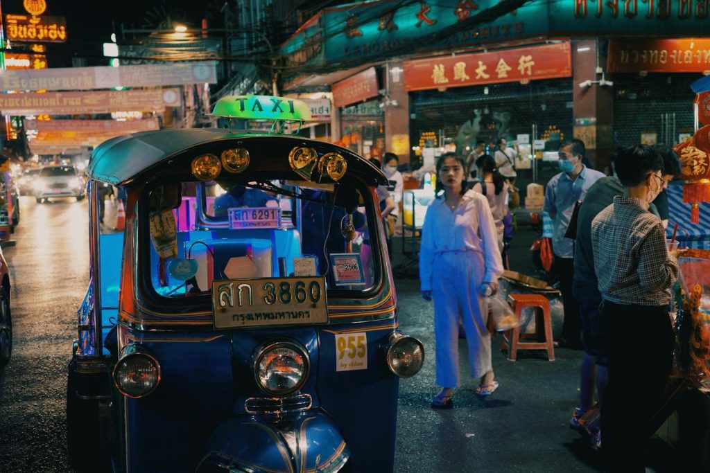 Illuminated street scene with motor scooter and pedestrians in busy night market area.