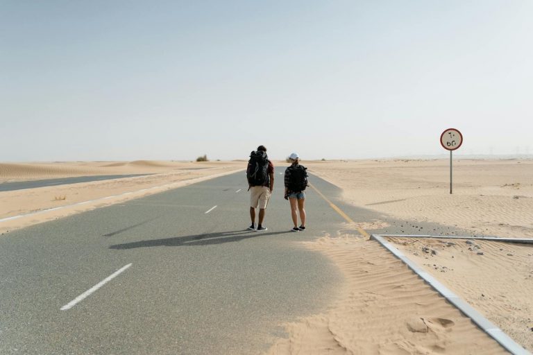 Zwei Backpacker wandern auf einer verlassenen Straße durch die Wüste