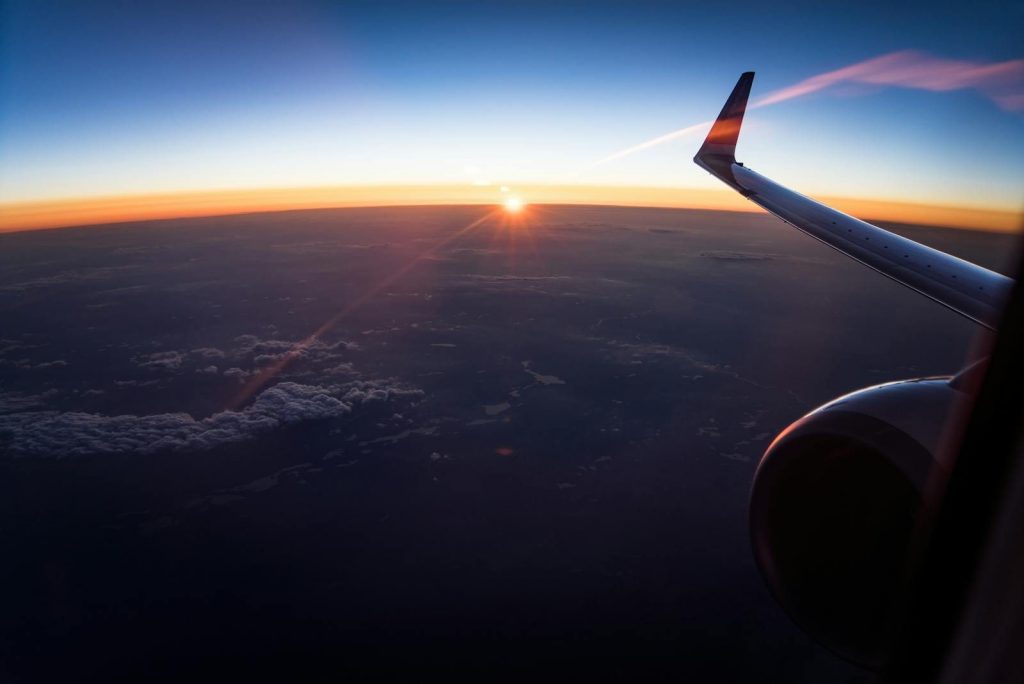 Flugzeugflügel aus dem Fenster mit Sonnenuntergang über den Wolken