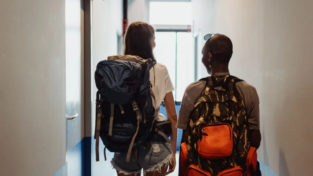 Zwei Backpackerinnen mit Reiserucksäcken auf dem Weg durch ein Hostel