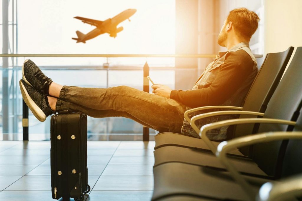 Mann sitzt im Flughafenterminal und blickt auf ein startendes Flugzeug