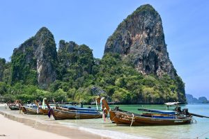 Longtail boats on the scenic Ao Nang Beach with limestone cliffs under a bright sky in Thailand.