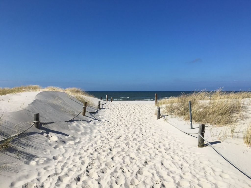 Sandiger Weg zum Strand unter blauem Himmel