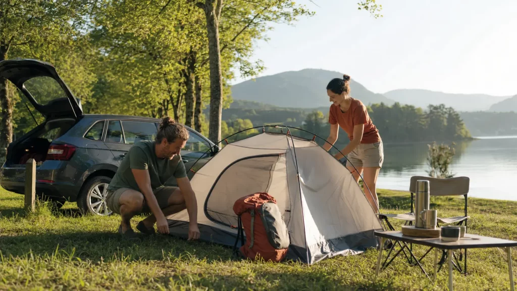 Paar baut beim Camping ein Zelt an einem Bergsee auf