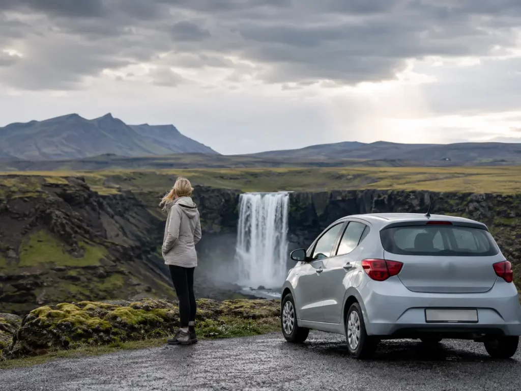 Reisende mit Mietwagen an einem Wasserfall in Island